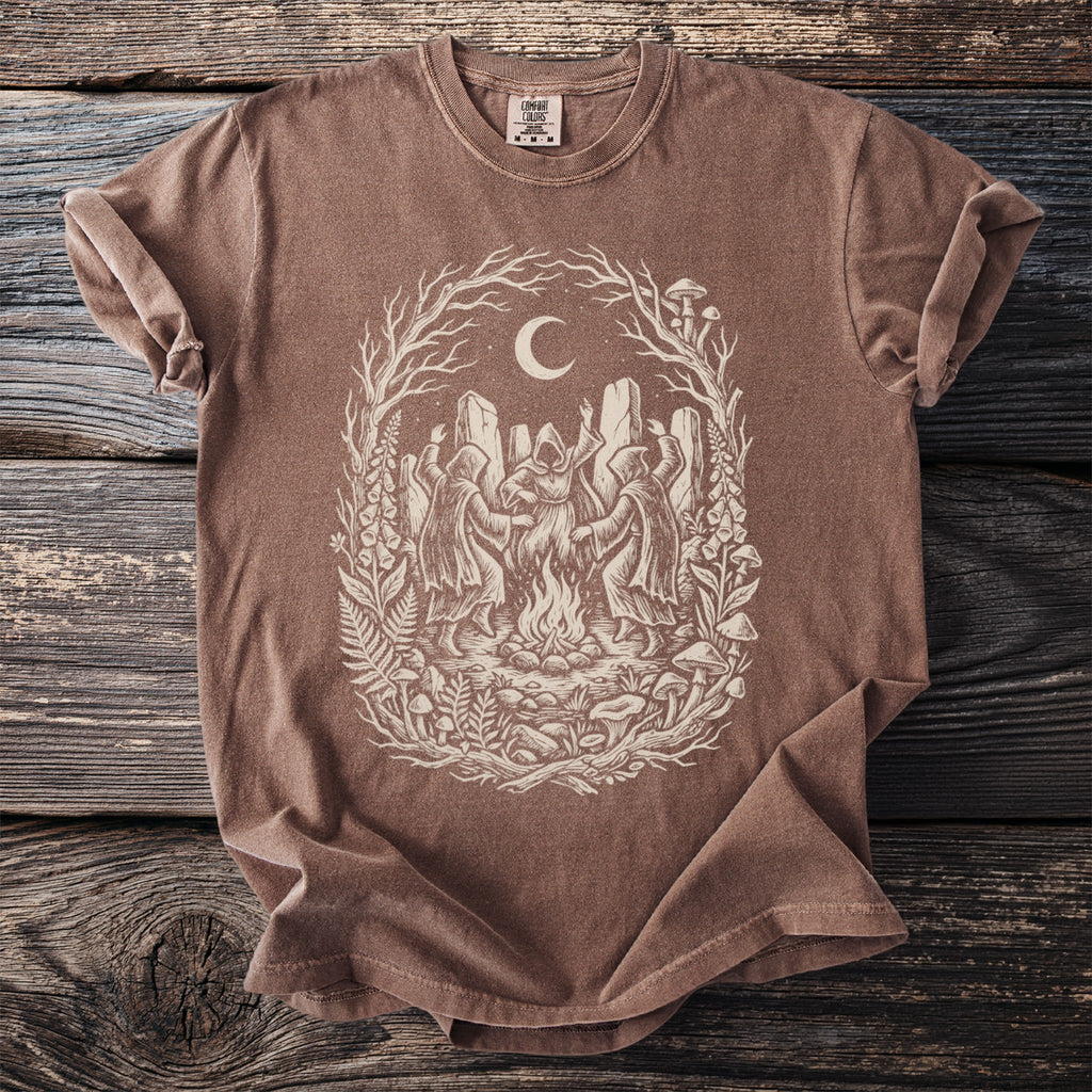 Brown t-shirt with screen print of figures dancing around a campfire under a moon.