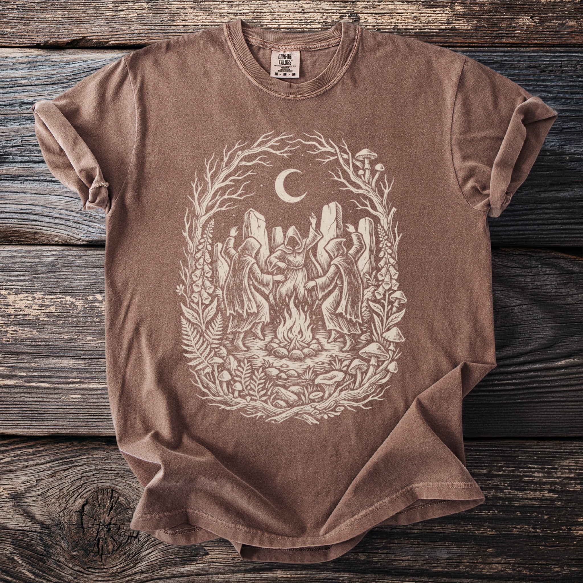 Brown t-shirt with screen print of figures dancing around a campfire under a moon.