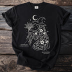 Black t-shirt with white line art of a witch holding mandrake above starry sky and crescent moon.
