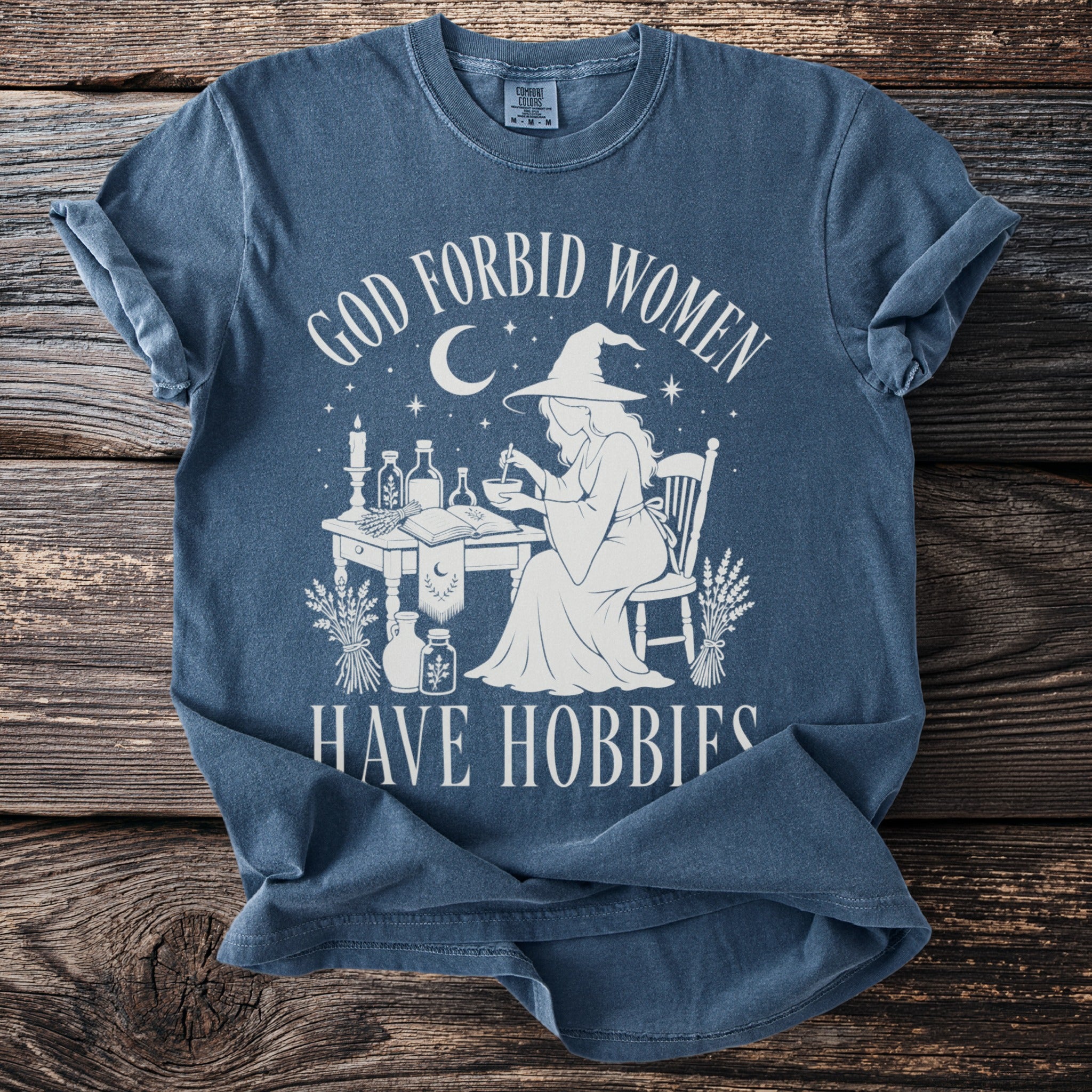 T-shirt with white graphic of witch at a table and text "GOD FORBID WOMEN HAVE HOBBIES".
