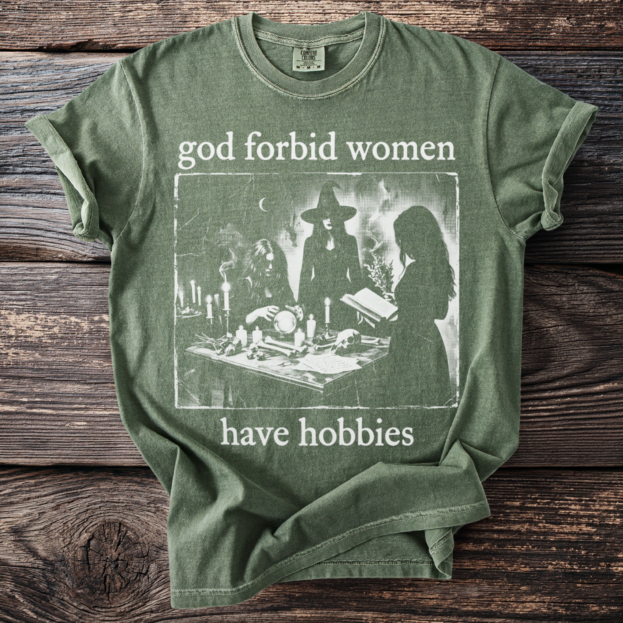 Green t-shirt with "god forbid women have hobbies" text and a witch illustration.