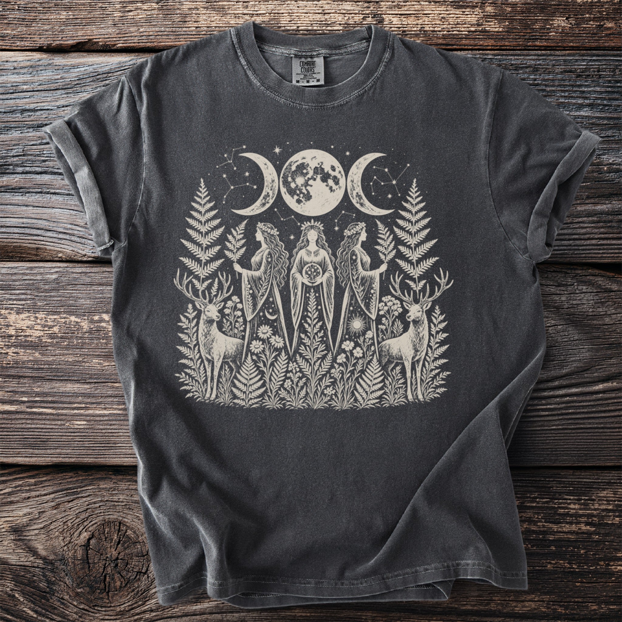 Dark t-shirt with cream graphic of triple moon, goddesses, and stags.
