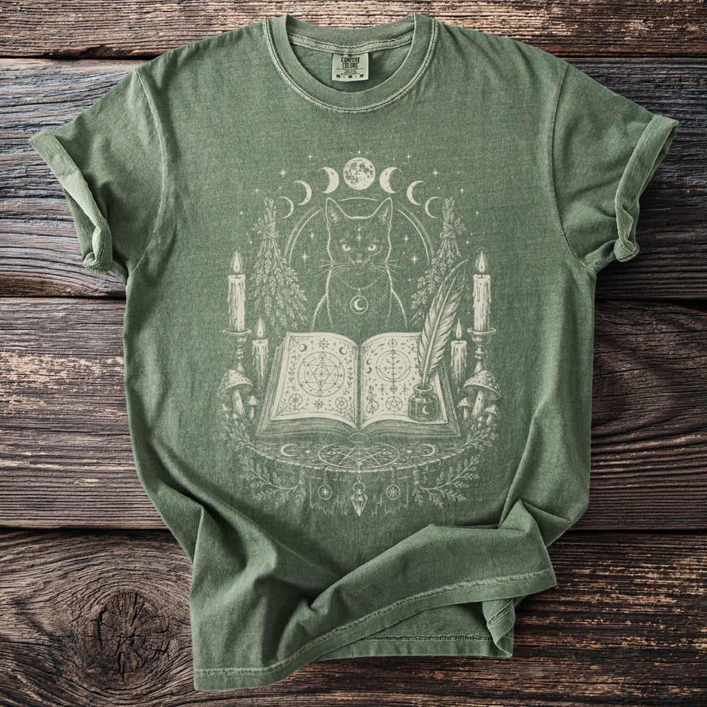 Green t-shirt with a cat, open book, candles, and moon phases design.