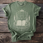 Green t-shirt with a cat, open book, candles, and moon phases design.