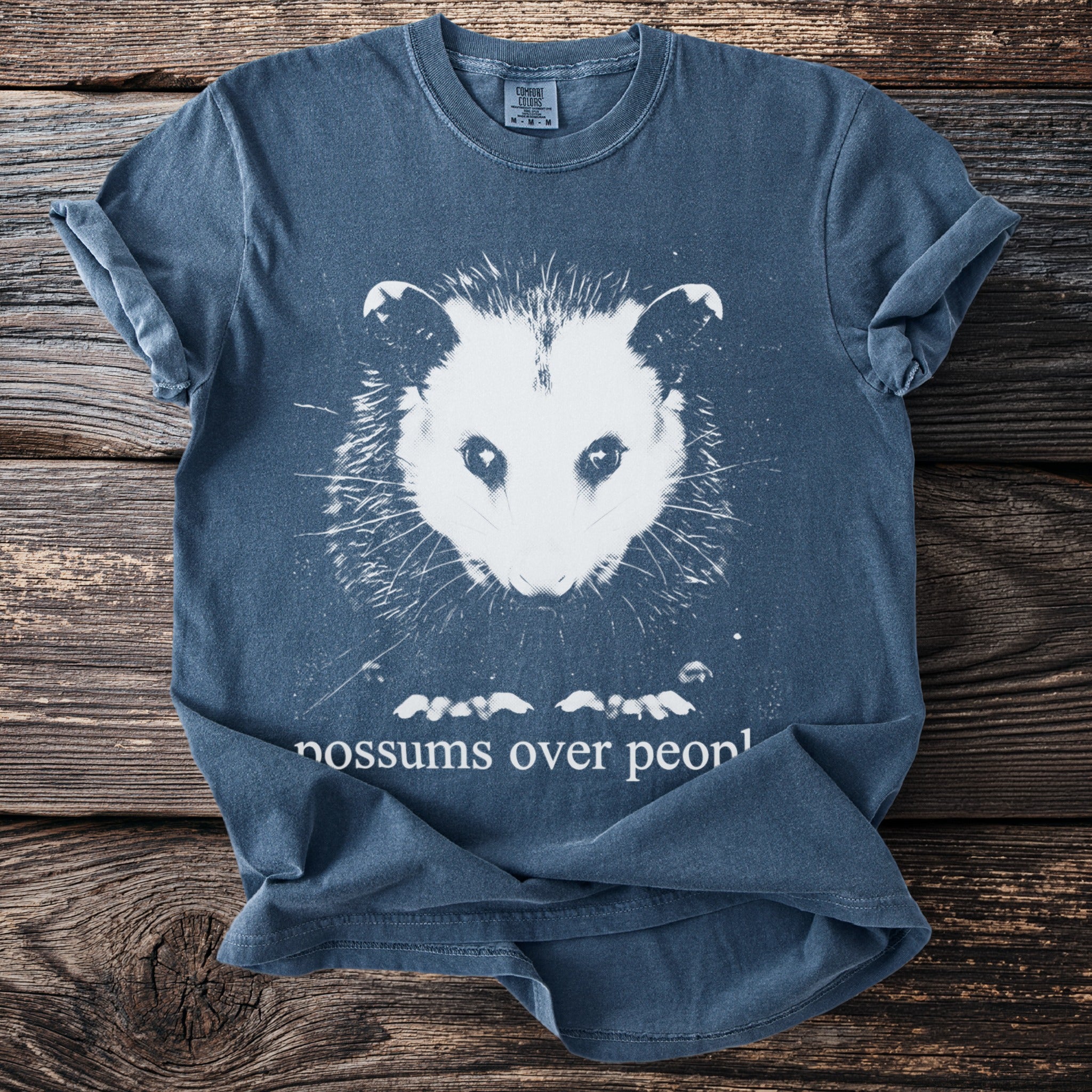 Blue t-shirt with white possum graphic and text "possums over peopl".