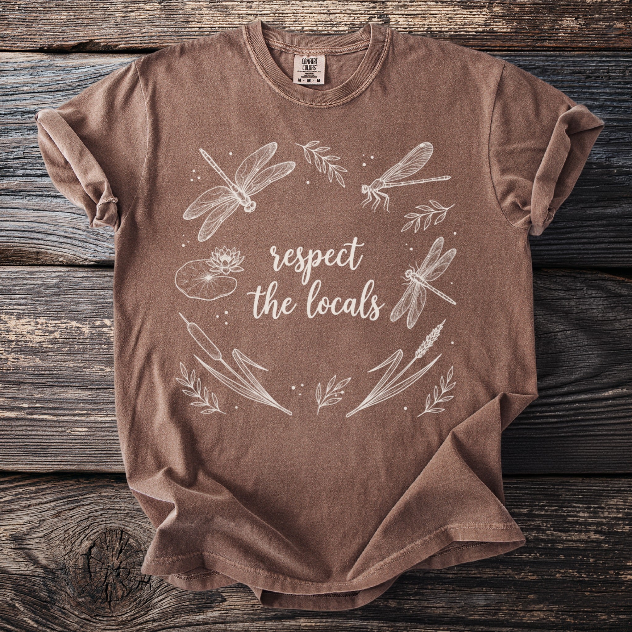 Brown t-shirt with white dragonfly and floral design reading "respect the locals".