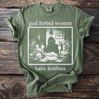 Green t-shirt with "god forbid women have hobbies" text and gothic illustration.