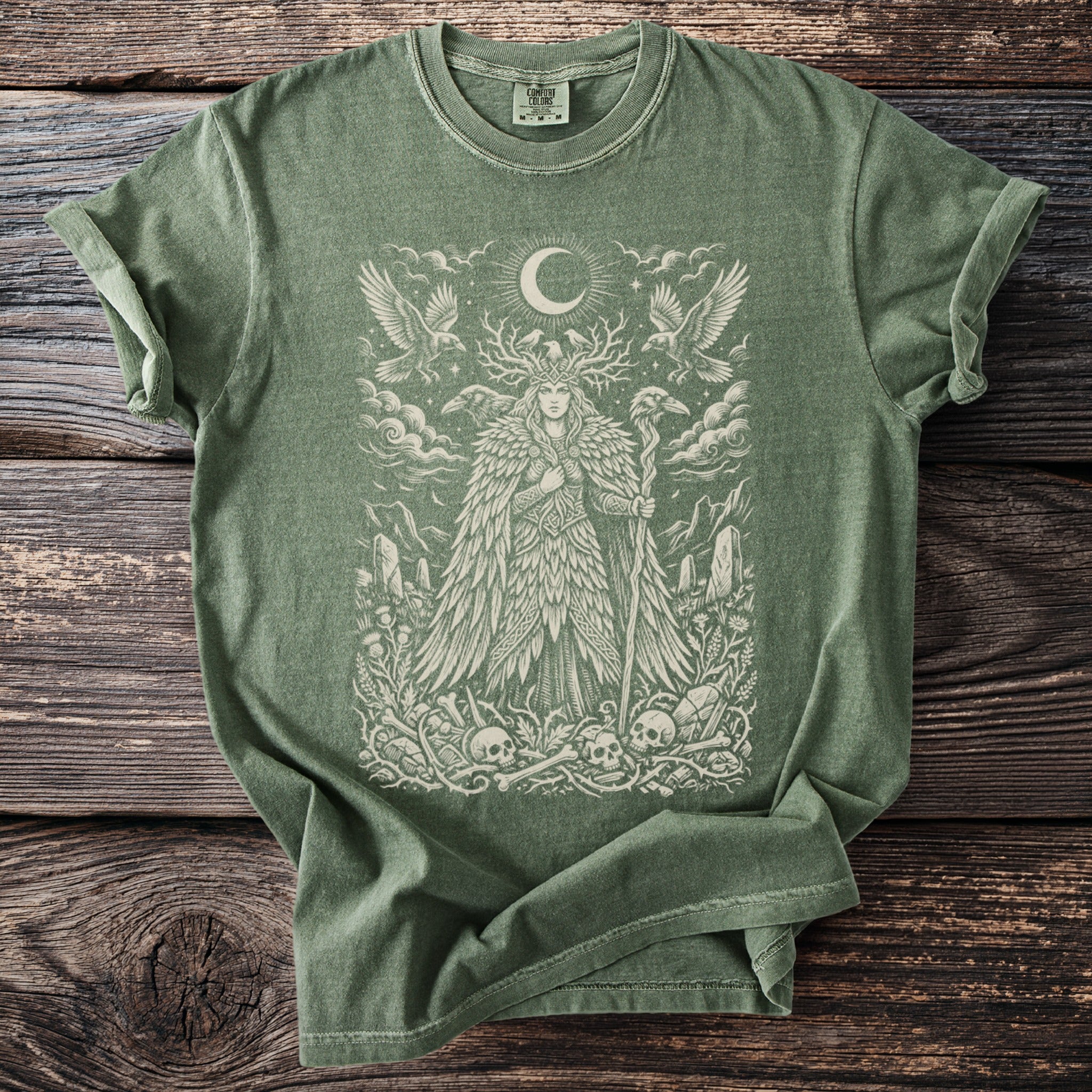 Sage green t-shirt with a detailed print of a mystical figure, birds, and skulls.
