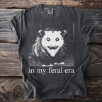 Dark gray t-shirt with a black and white print of an angry opossum and text "in my feral era."