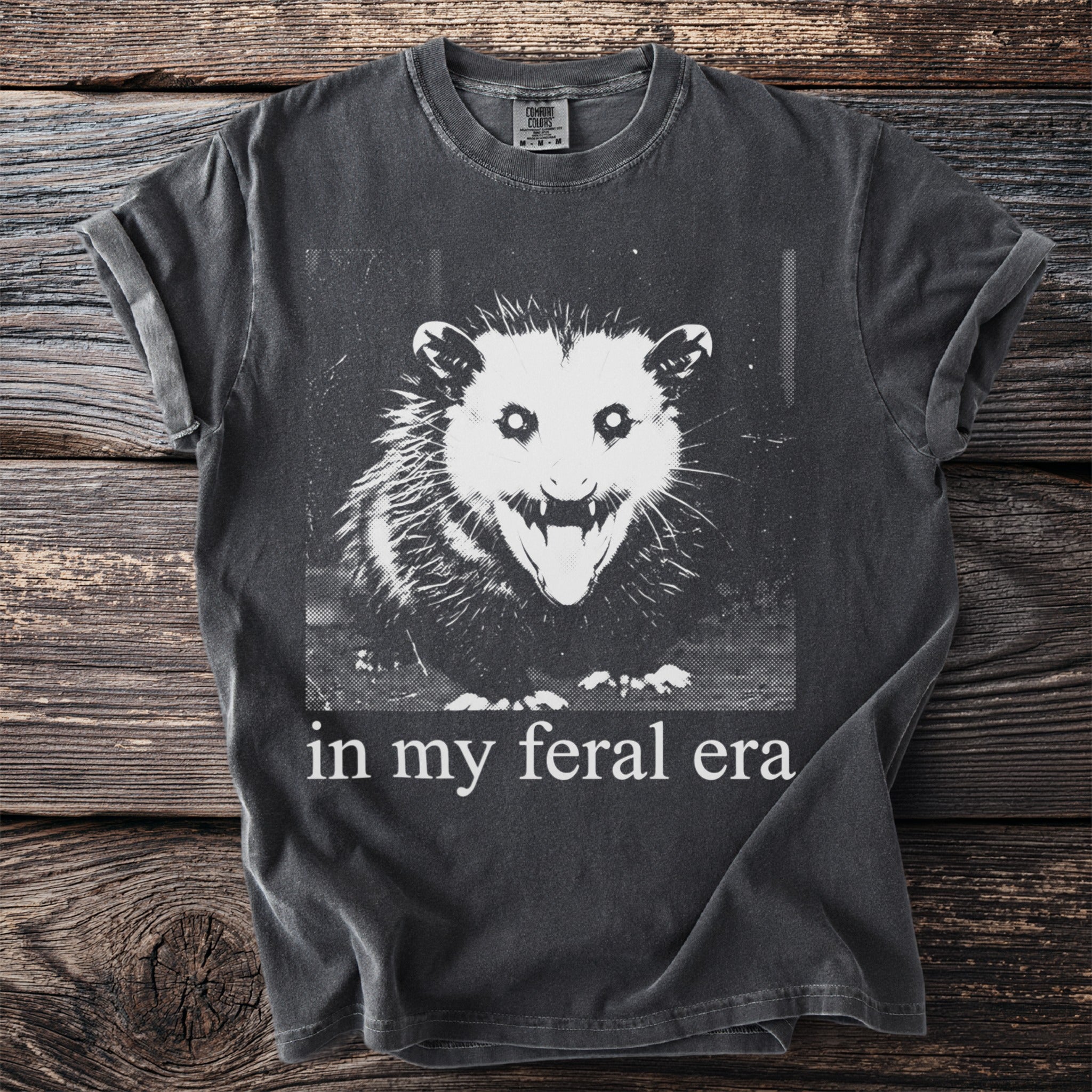 Dark gray t-shirt with a black and white print of an angry opossum and text "in my feral era."