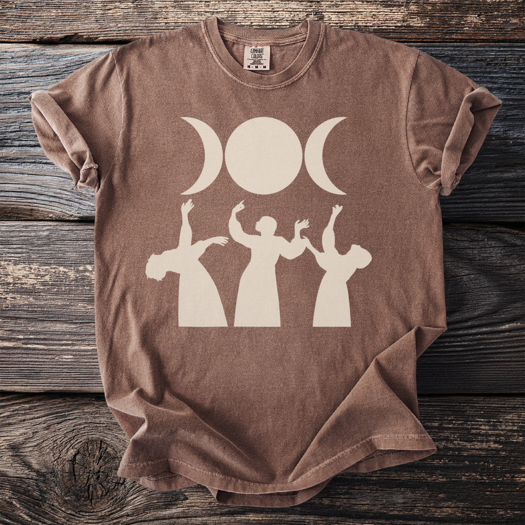 Brown t-shirt with triple moon goddess and dancing figures graphic.