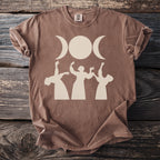 Brown t-shirt with triple moon goddess and dancing figures graphic.