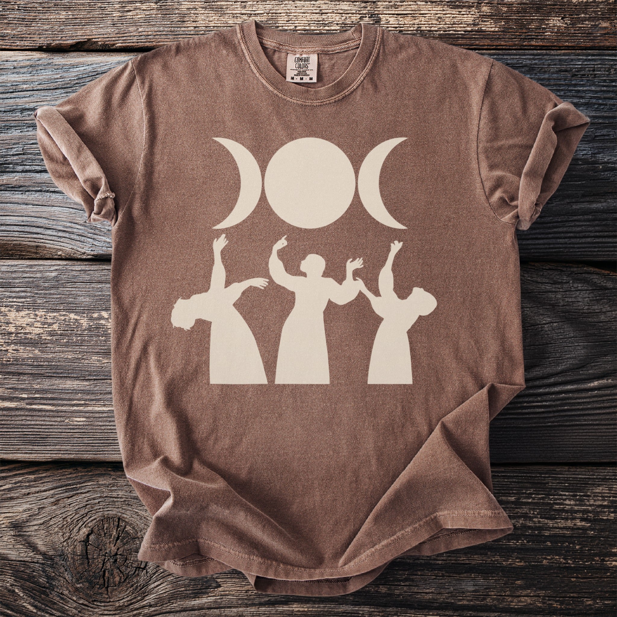 Brown t-shirt with triple moon goddess and dancing figures graphic.
