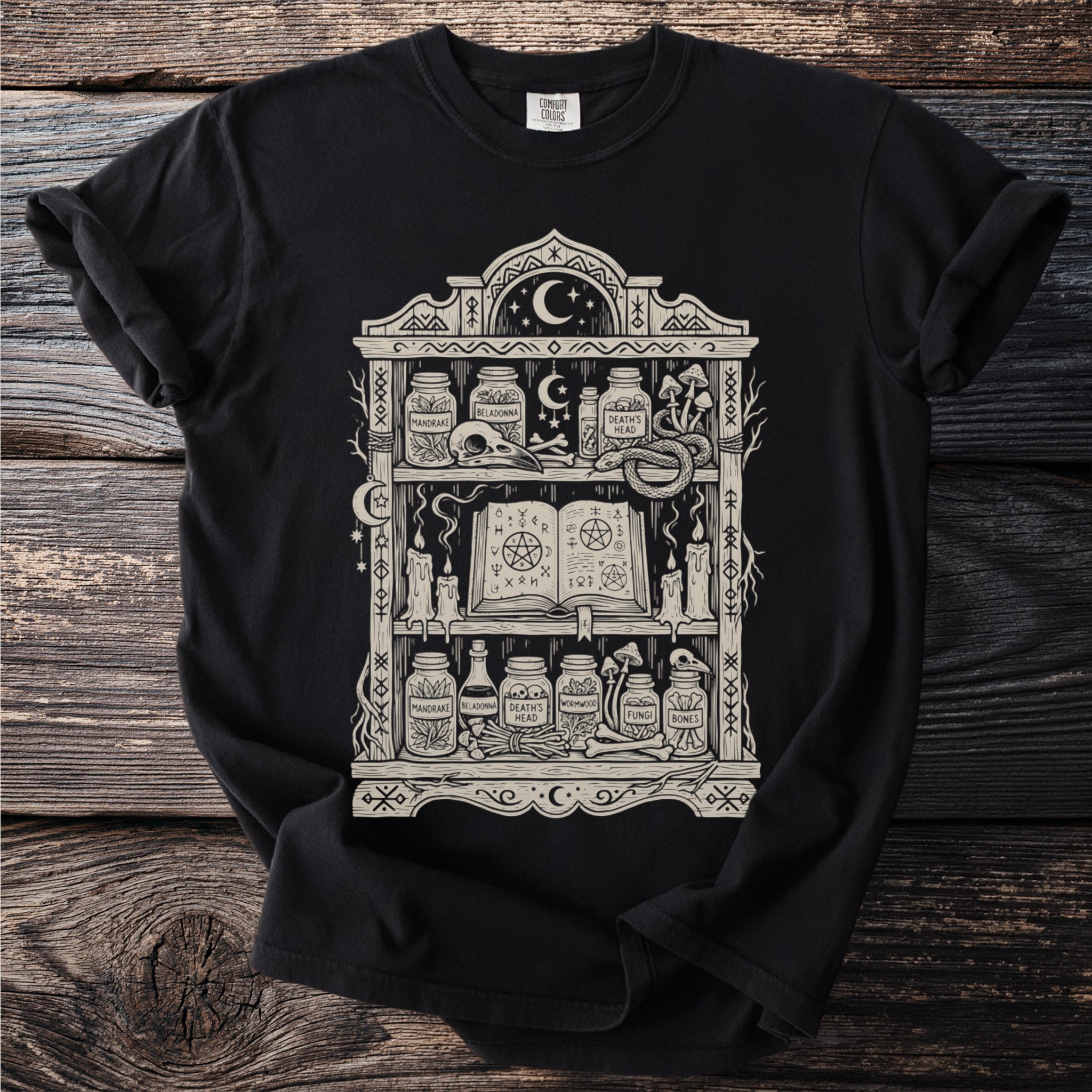 Black t-shirt with a cream graphic of a mystic bookshelf and occult items.