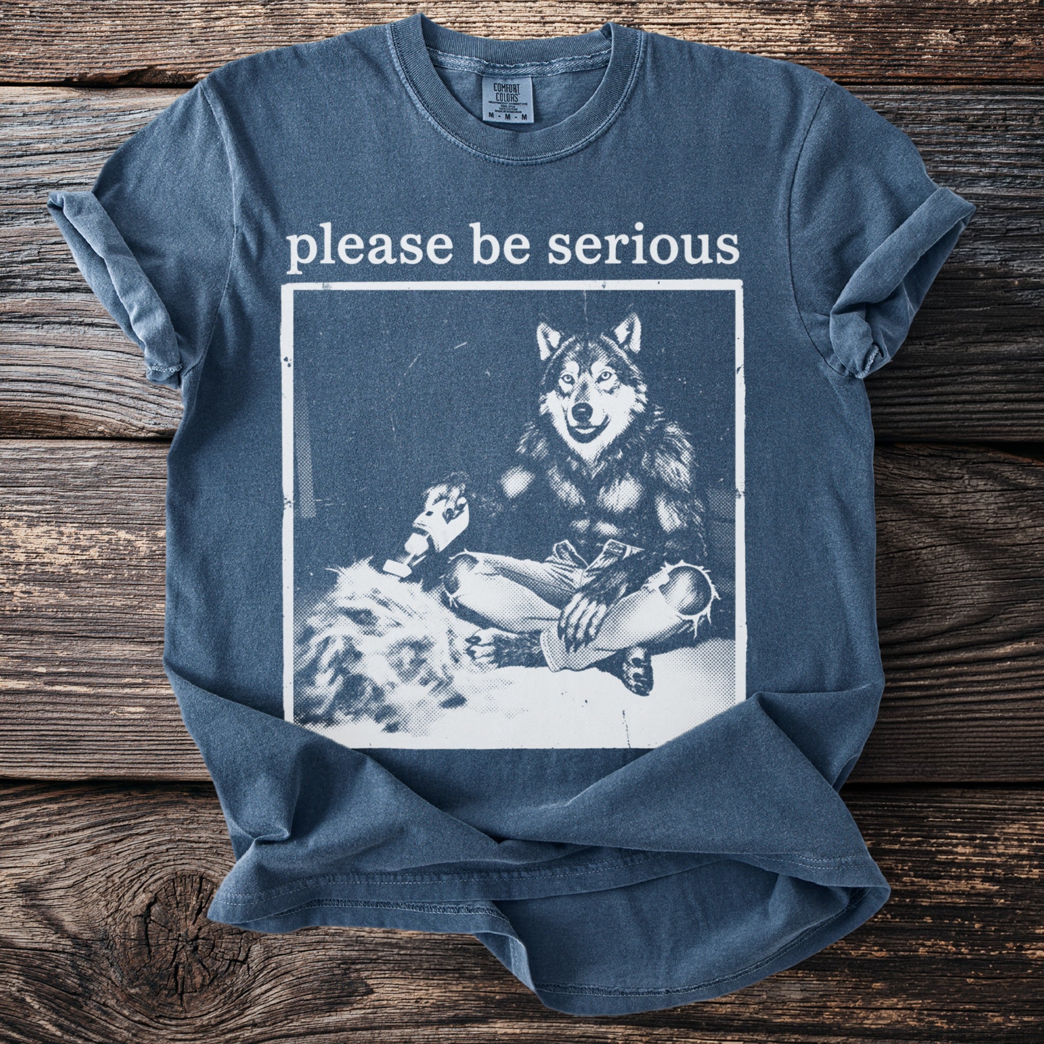 Blue t-shirt with white text "please be serious" above a wolf graphic.