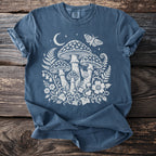 Blue t-shirt with white graphic of mushrooms, moon, stars, butterfly, and snail.