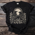 Black t-shirt with linocut style art of two ravens on a branch with a sun and stars.