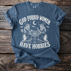 Blue t-shirt with "God Forbid Women Have Hobbies" text, two witches, and a cat.