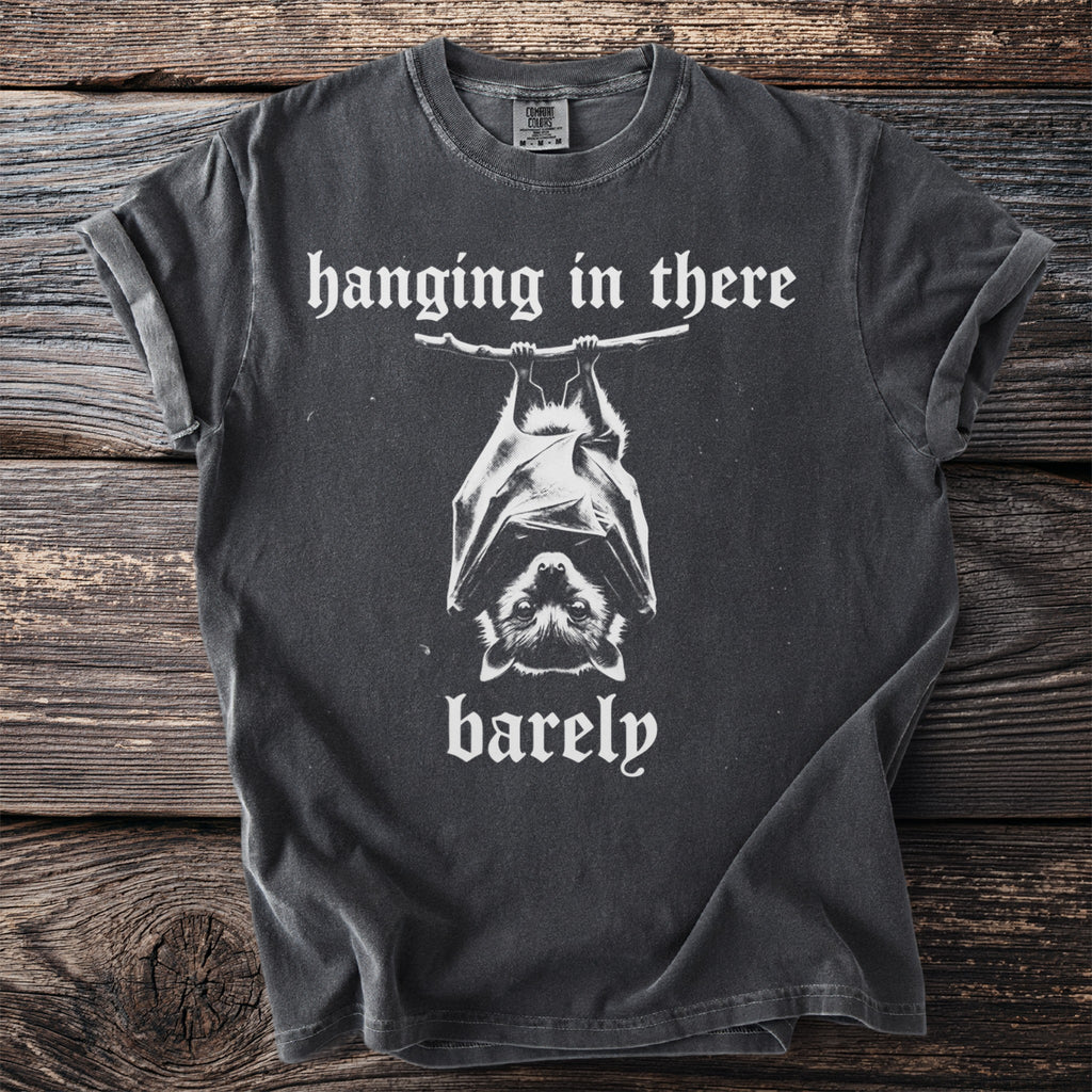Dark t-shirt with white text "hanging in there barely" and a bat graphic.