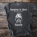 Dark t-shirt with white text "hanging in there barely" and a bat graphic.