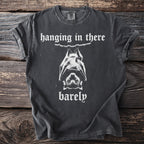 Dark t-shirt with white text "hanging in there barely" and a bat graphic.