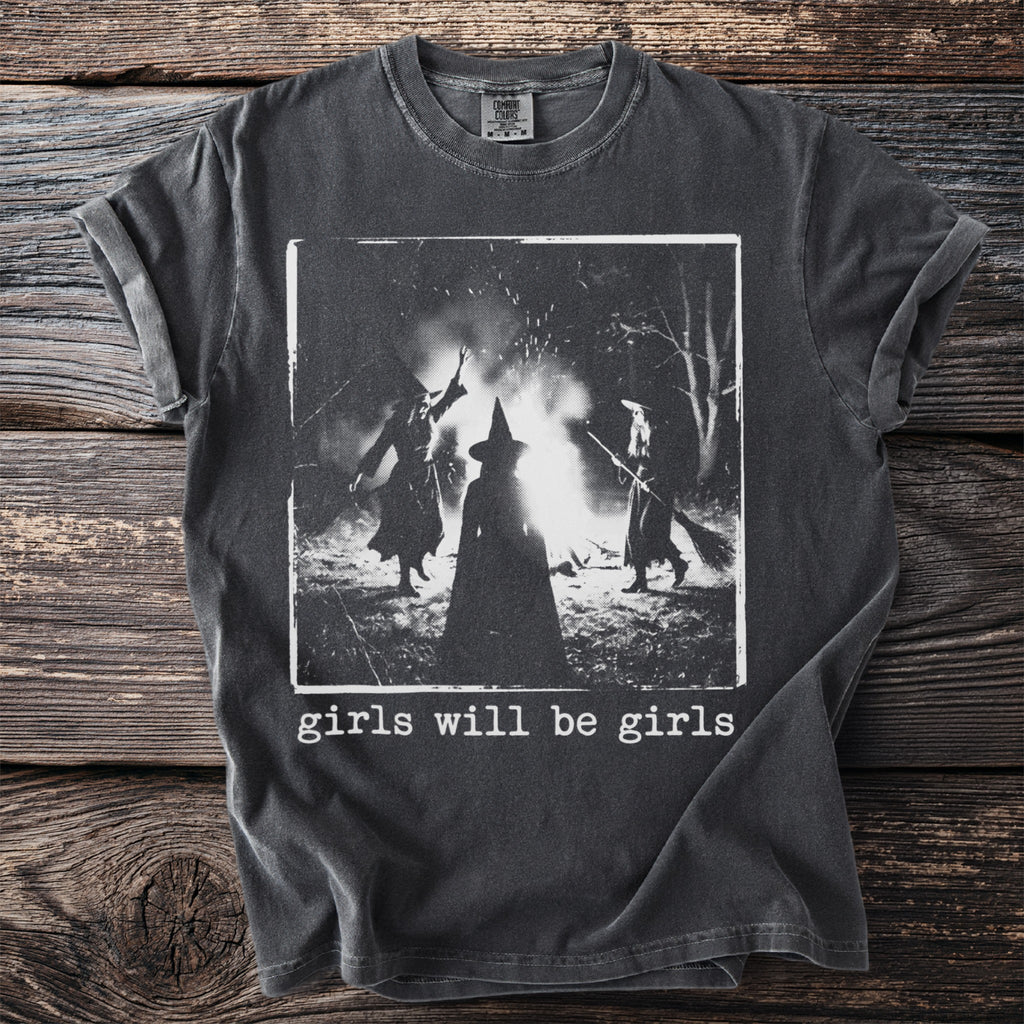 Dark gray t-shirt with a graphic of three witches around a bonfire and the text "girls will be girls".