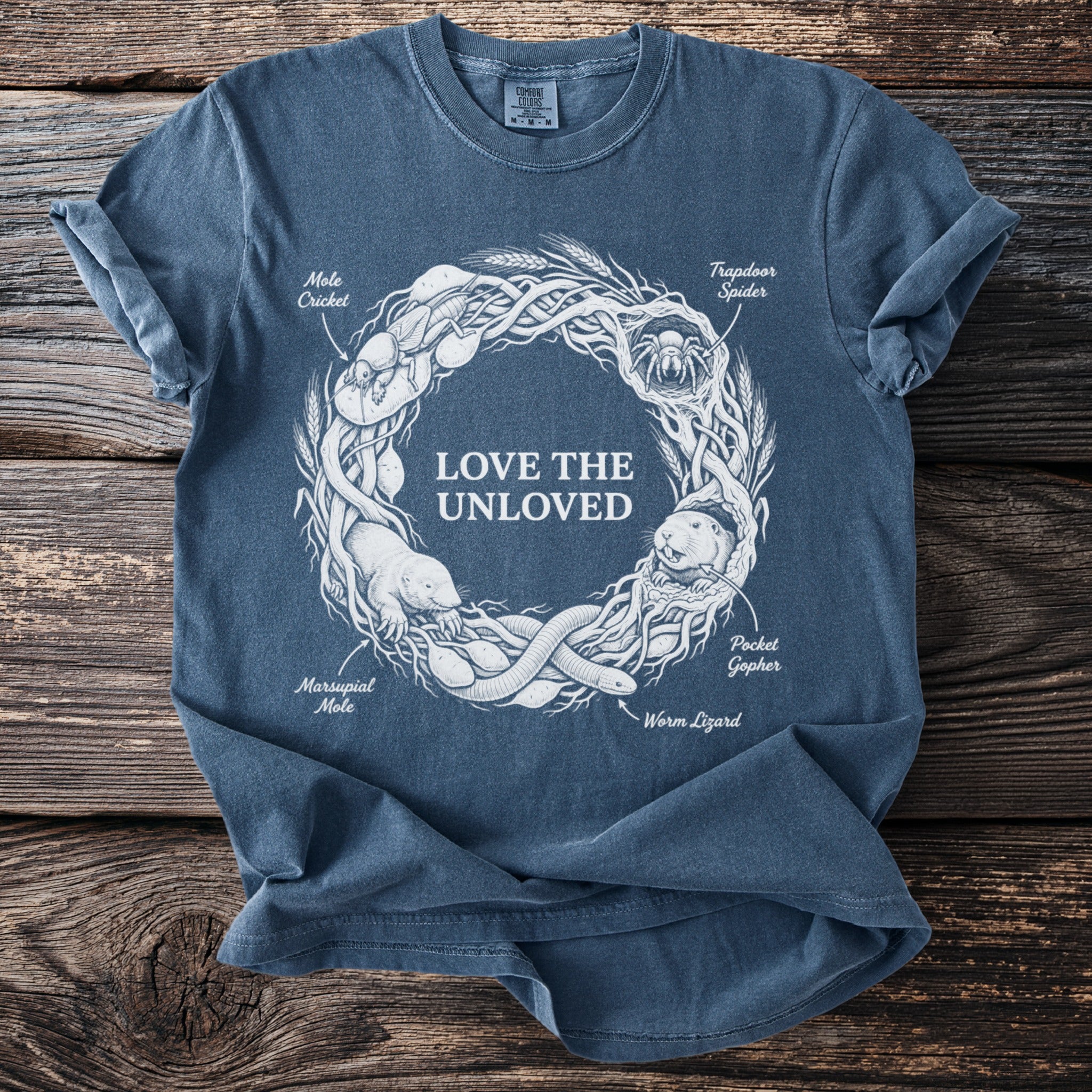 Blue t-shirt with central graphic "LOVE THE UNLOVED" and surrounding illustrated creatures.