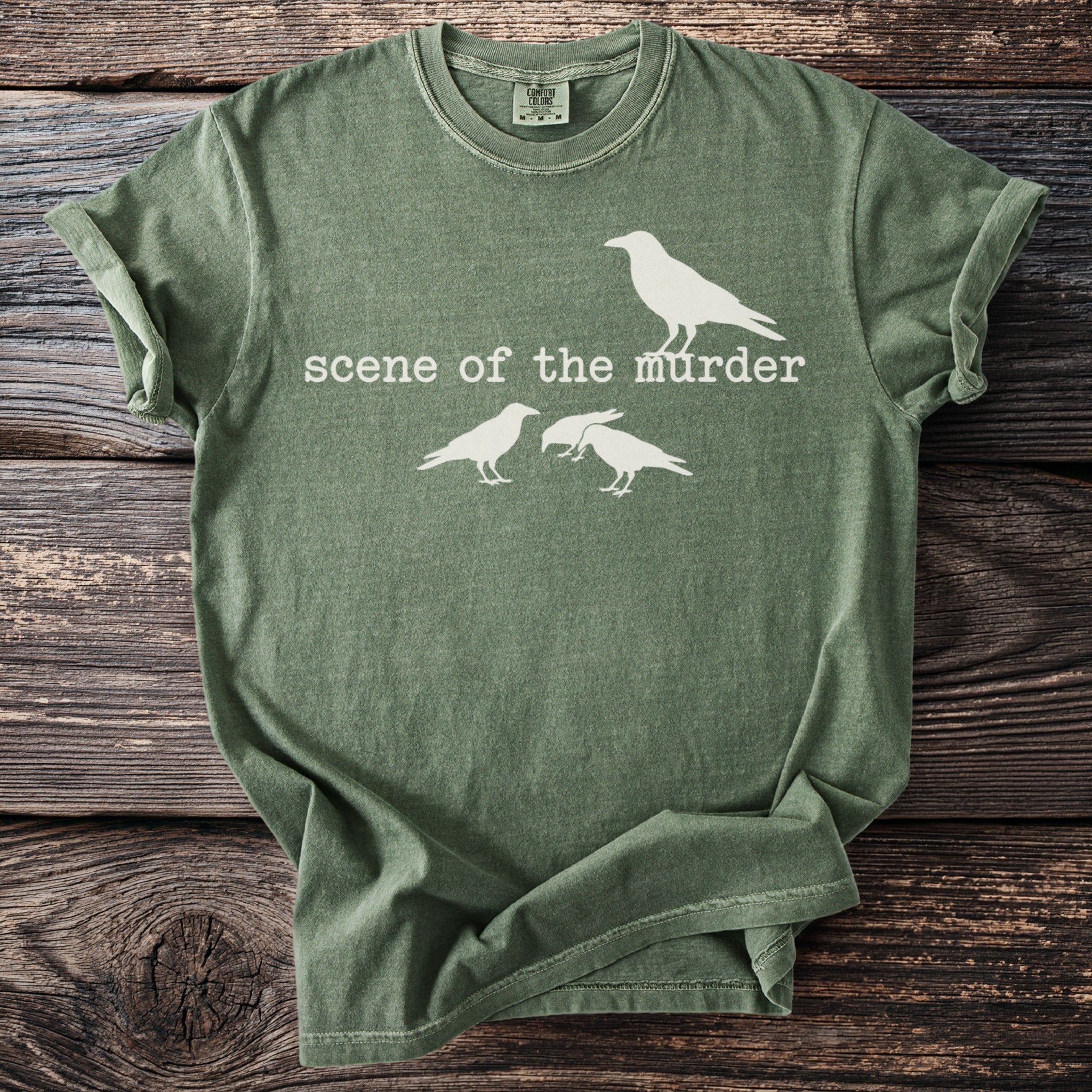 Green t-shirt with white text "scene of the murder" and three crows.