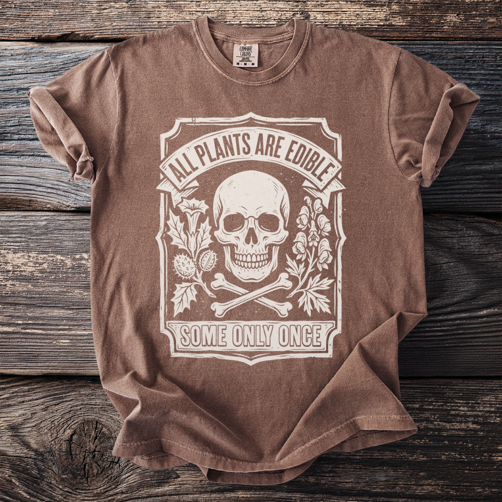 Brown t-shirt with white graphic of skull, bones, and plants; text says "All Plants Are Edible Some Only Once".