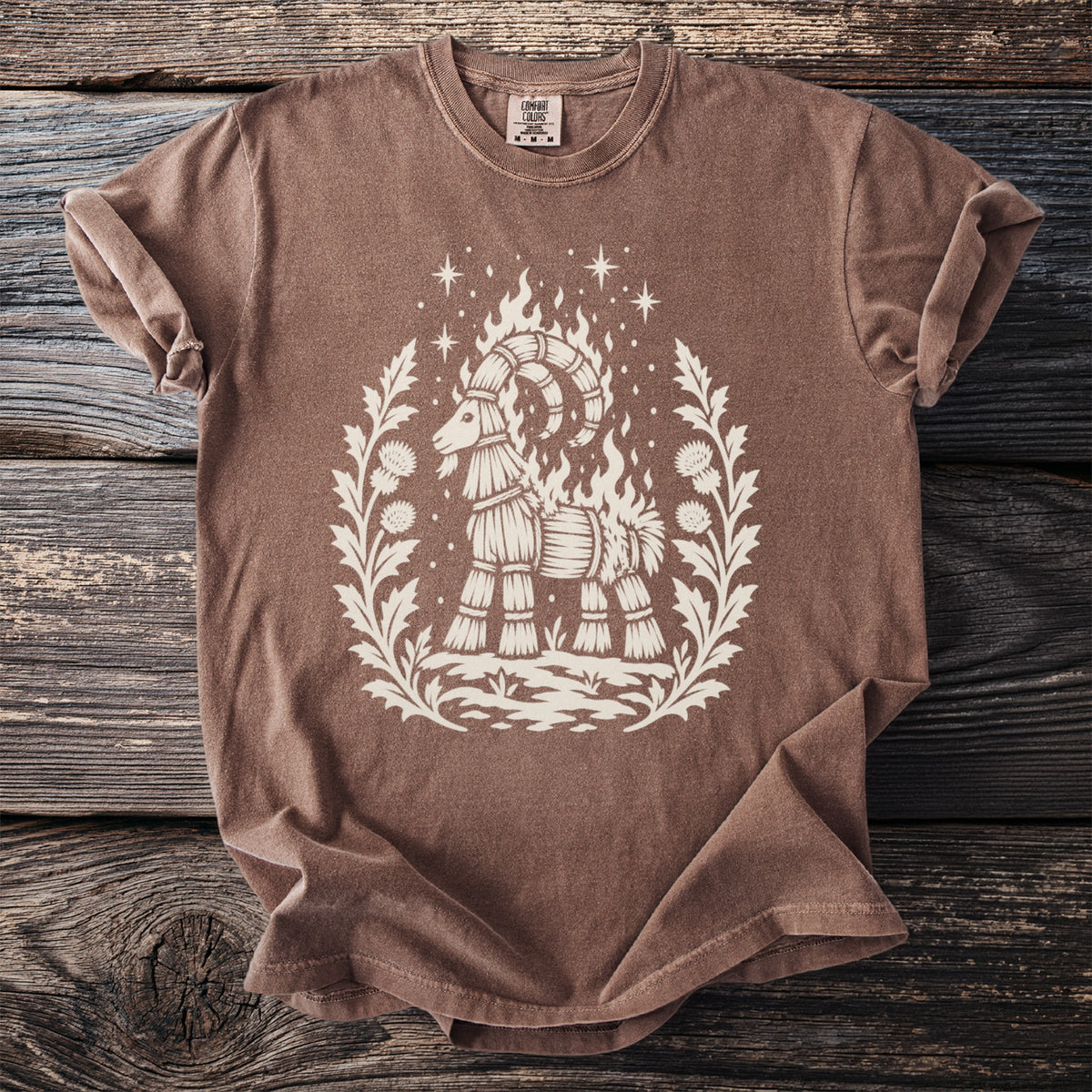 Brown t-shirt with cream-colored design of a burning straw goat surrounded by plants.
