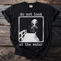 Black t-shirt with "do not look at the water" and a monster emerging from water.