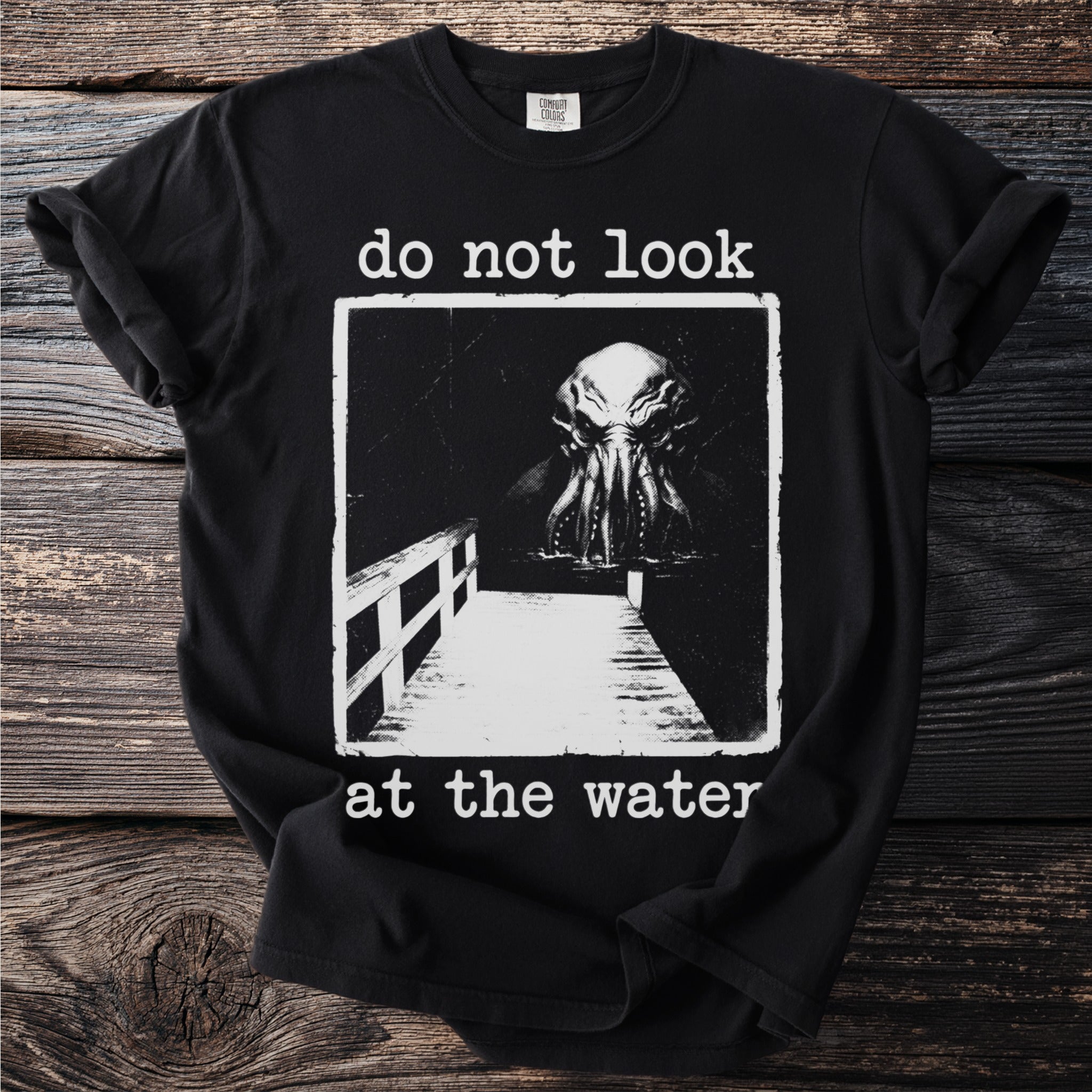 Black t-shirt with "do not look at the water" and a monster emerging from water.