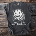 Dark gray t-shirt with white print of a snarling opossum and text "in my feral era".