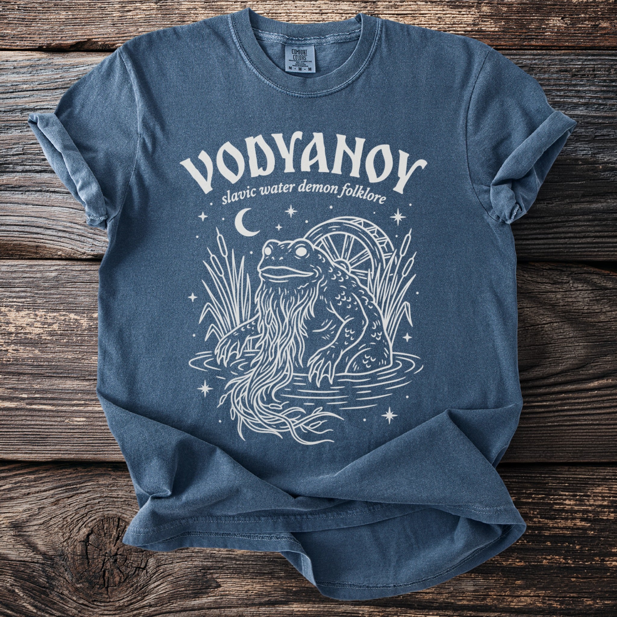 Blue t-shirt with white illustration "Vodyanoy slavic water demon folklore" and a frog.