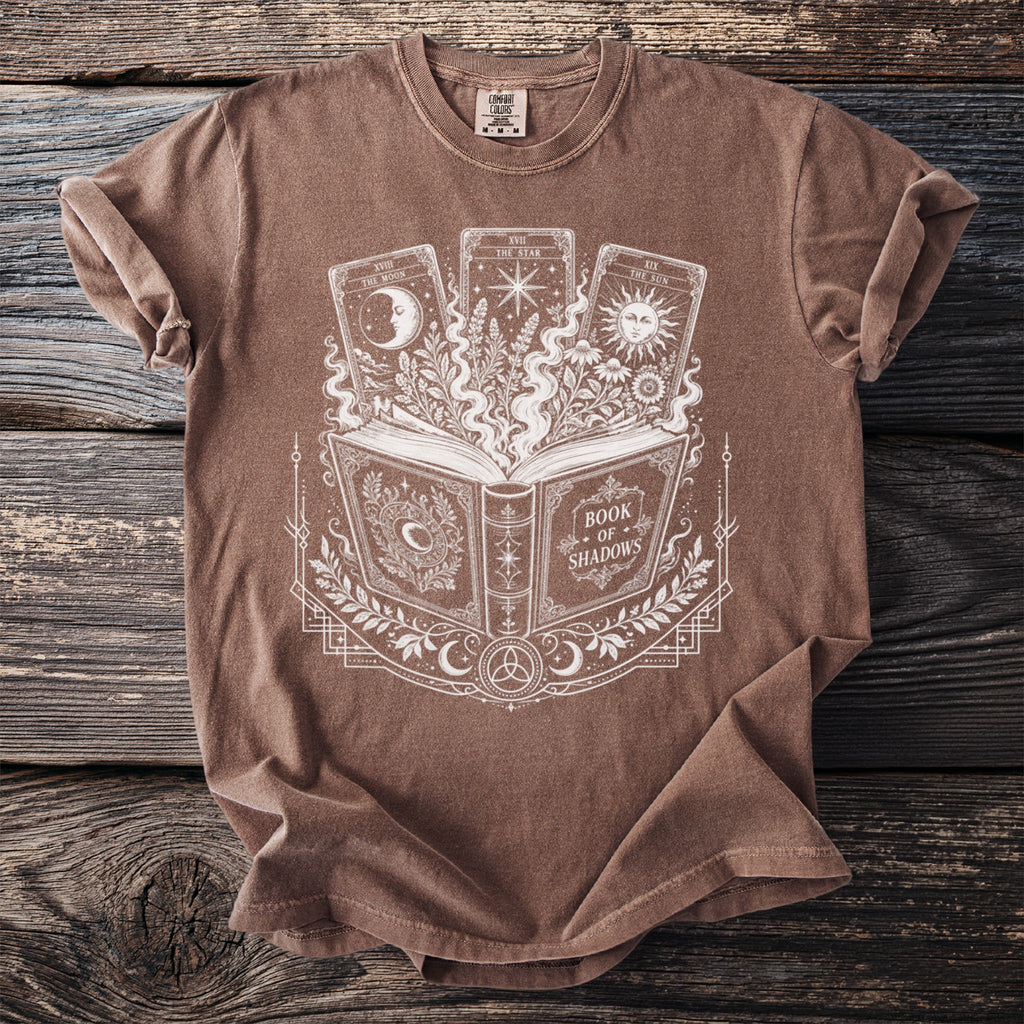 Brown t-shirt with white print of an open book titled "Book of Shadows" and three tarot cards.
