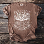 Brown t-shirt with white print of an open book titled "Book of Shadows" and three tarot cards.