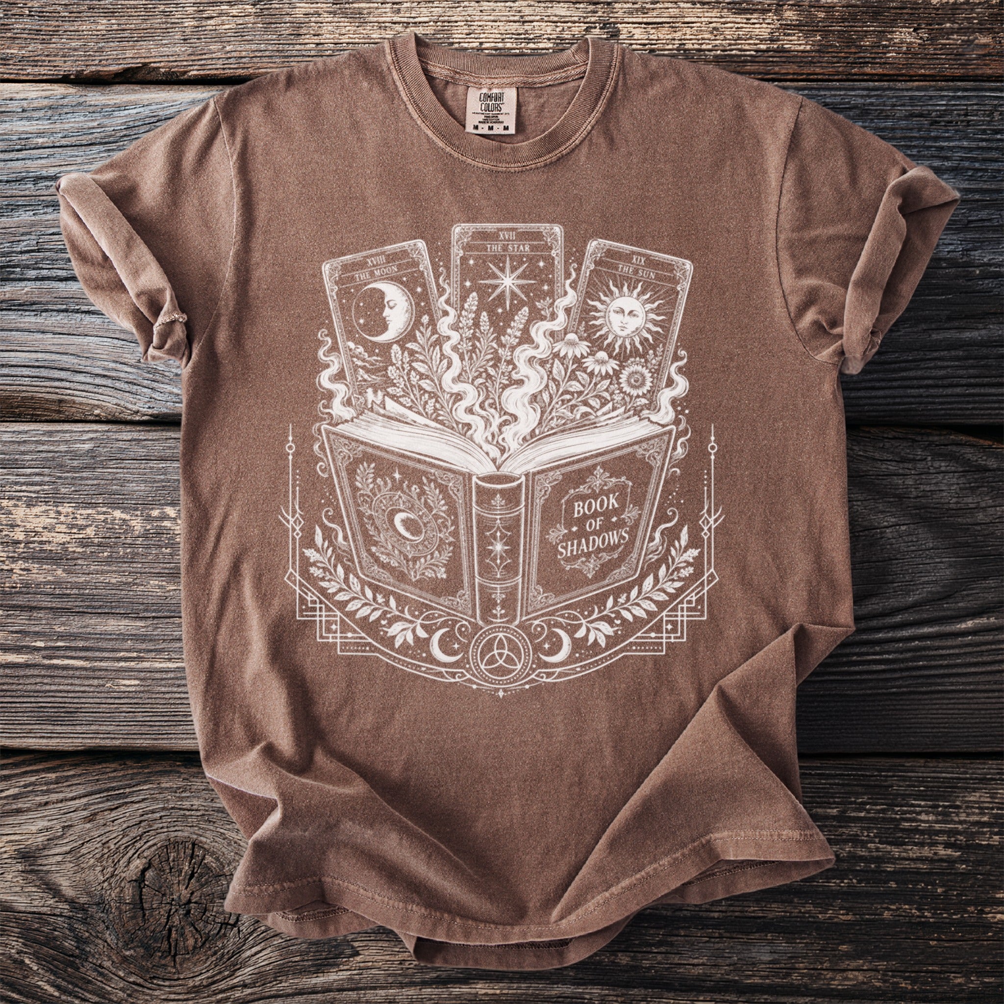 Brown t-shirt with white print of an open book titled "Book of Shadows" and three tarot cards.