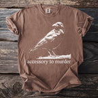 Brown t-shirt with graphic of a raven and text "accessory to murder".