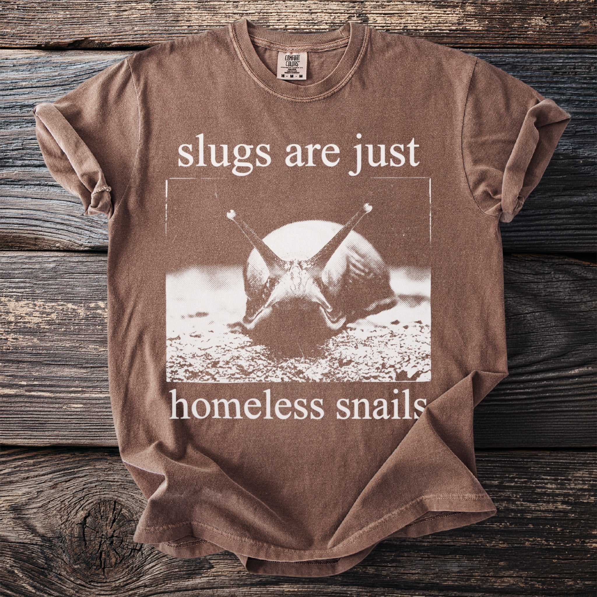 Brown t-shirt with a close-up snail graphic and text reading "slugs are just homeless snails."