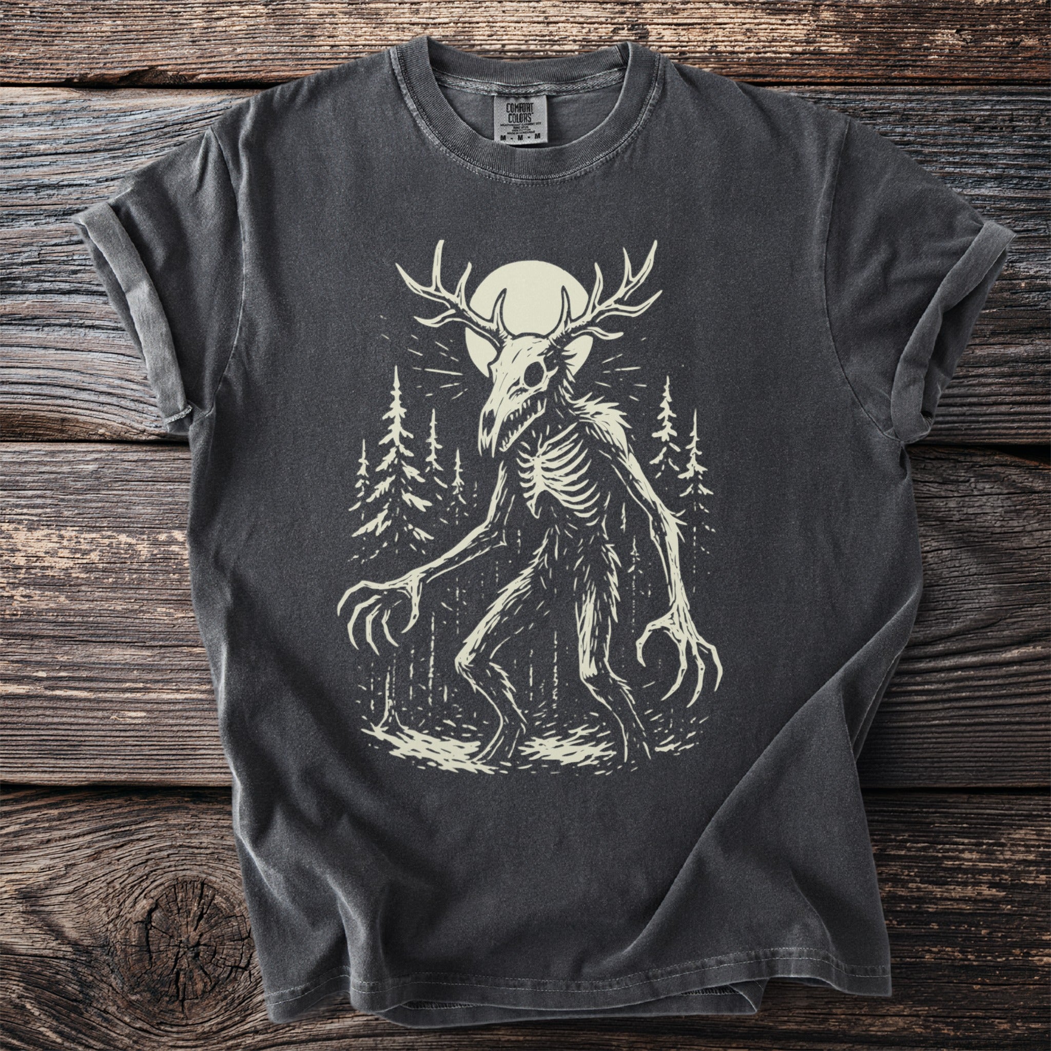 Dark grey t-shirt with a skeletal creature with antlers and long claws in a forest.
