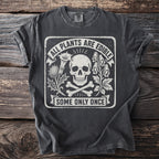 Dark t-shirt with a skull, crossbones, plants, and text "ALL PLANTS ARE EDIBLE SOME ONLY ONCE".