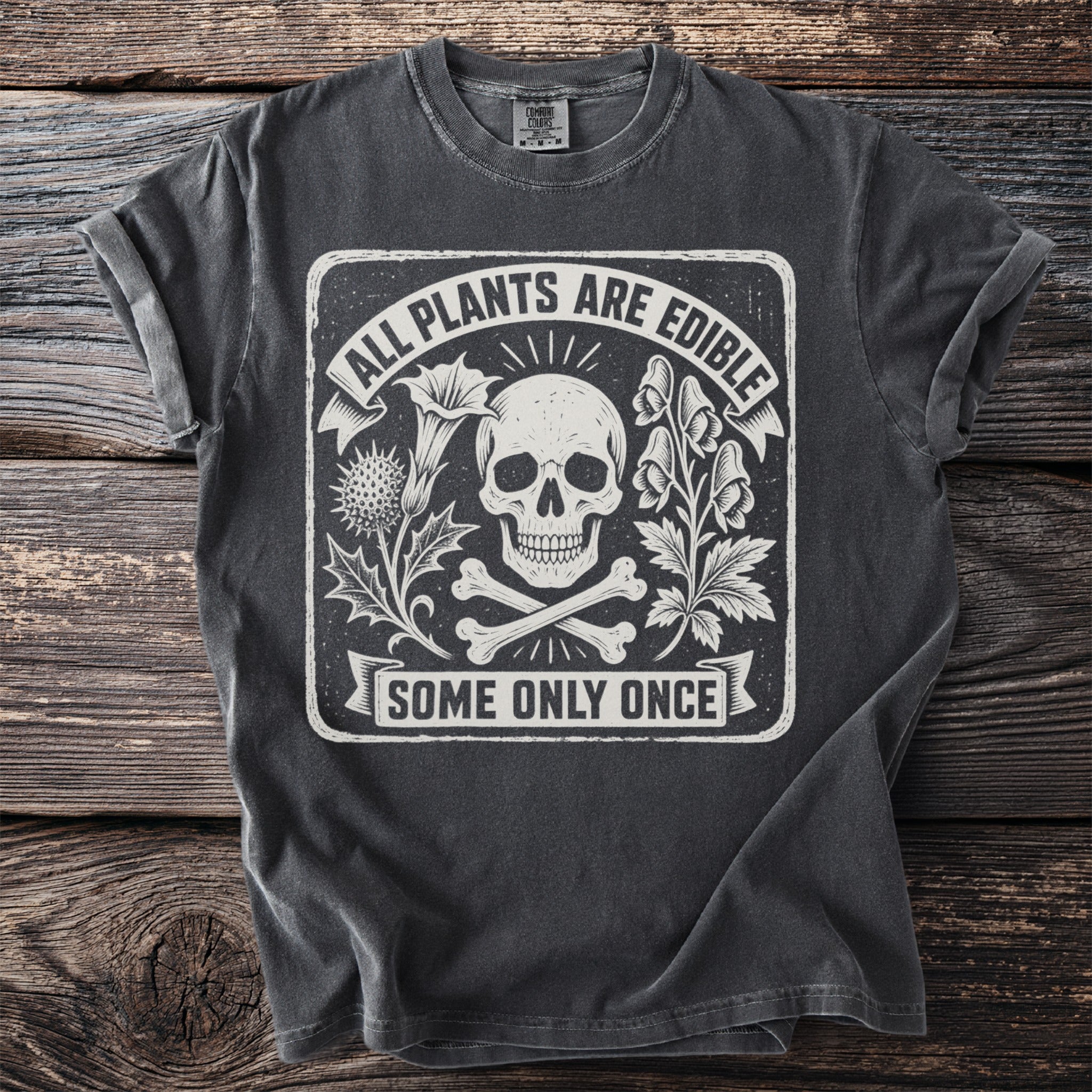 Dark t-shirt with a skull, crossbones, plants, and text "ALL PLANTS ARE EDIBLE SOME ONLY ONCE".