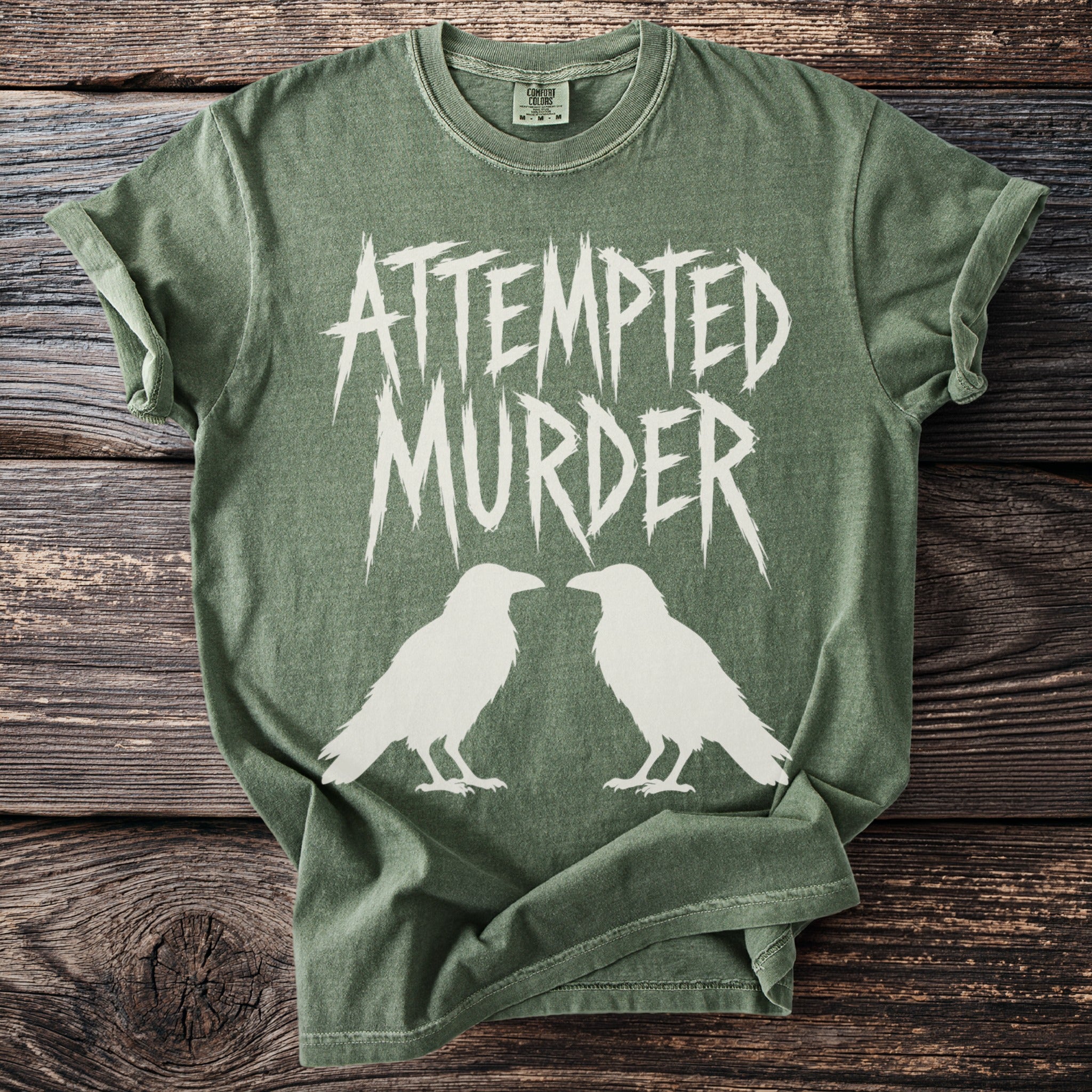 Olive green t-shirt with white "ATTEMPTED MURDER" text and two white raven silhouettes.