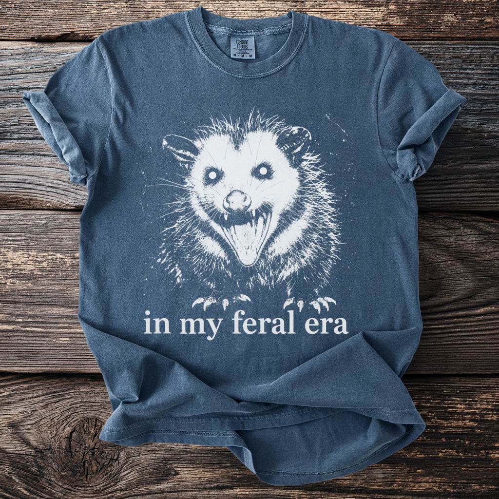 Blue t-shirt with a graphic of a screaming opossum and text "in my feral era".