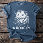 Blue t-shirt with a graphic of a screaming opossum and text "in my feral era".