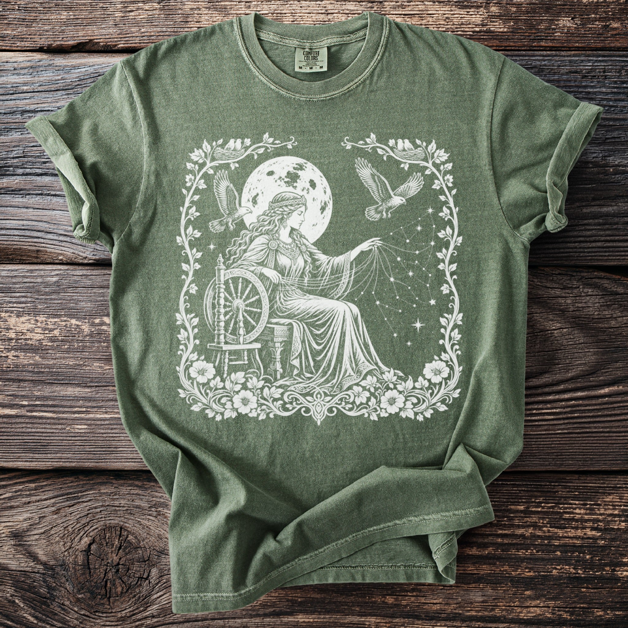 Olive green t-shirt with white graphic of woman spinning stars with eagles and moon overhead.