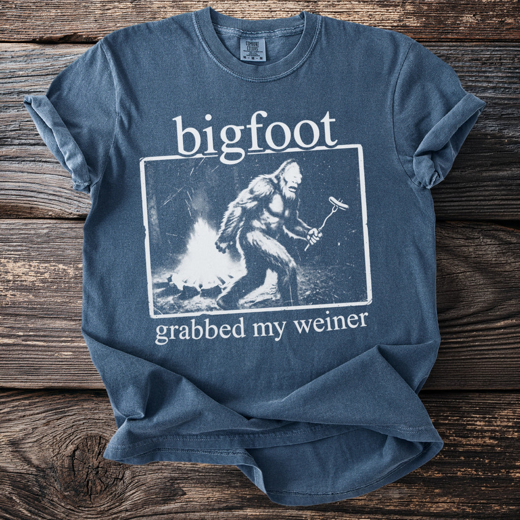 Blue t-shirt with Bigfoot around a campfire holding a hot dog skewer.