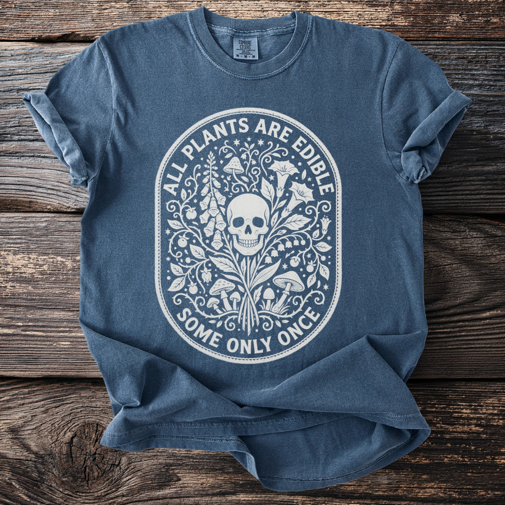 Blue t-shirt with white graphic of skull, plants, and mushrooms, text "ALL PLANTS ARE EDIBLE SOME ONLY ONCE".