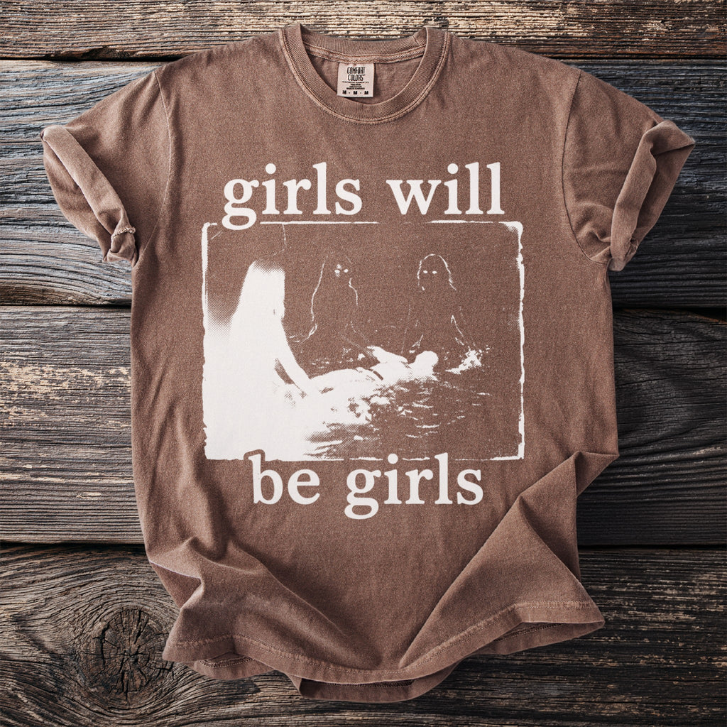 Brown t-shirt with white text "girls will be girls" and abstract graphic.