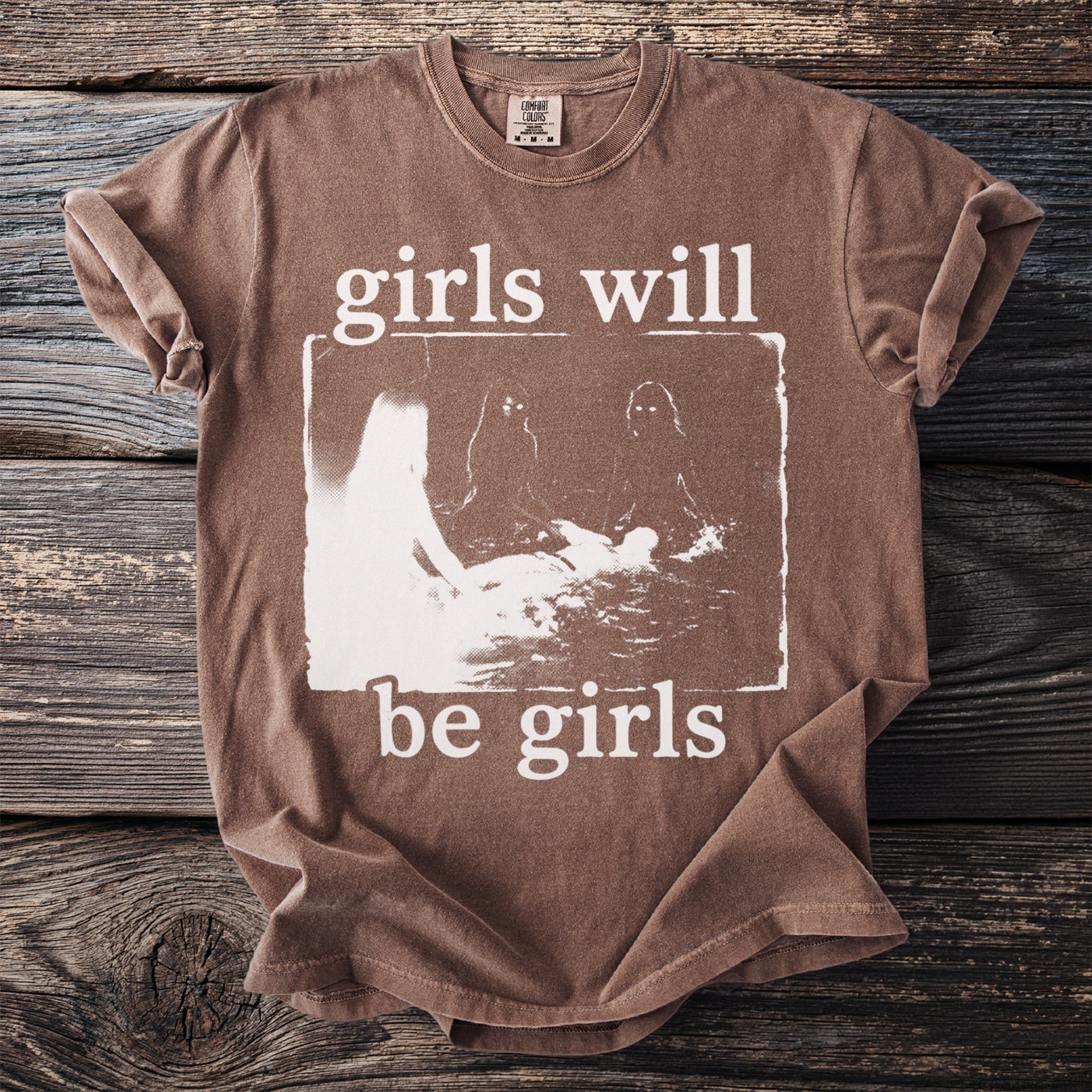 Brown t-shirt with white text "girls will be girls" and abstract graphic.